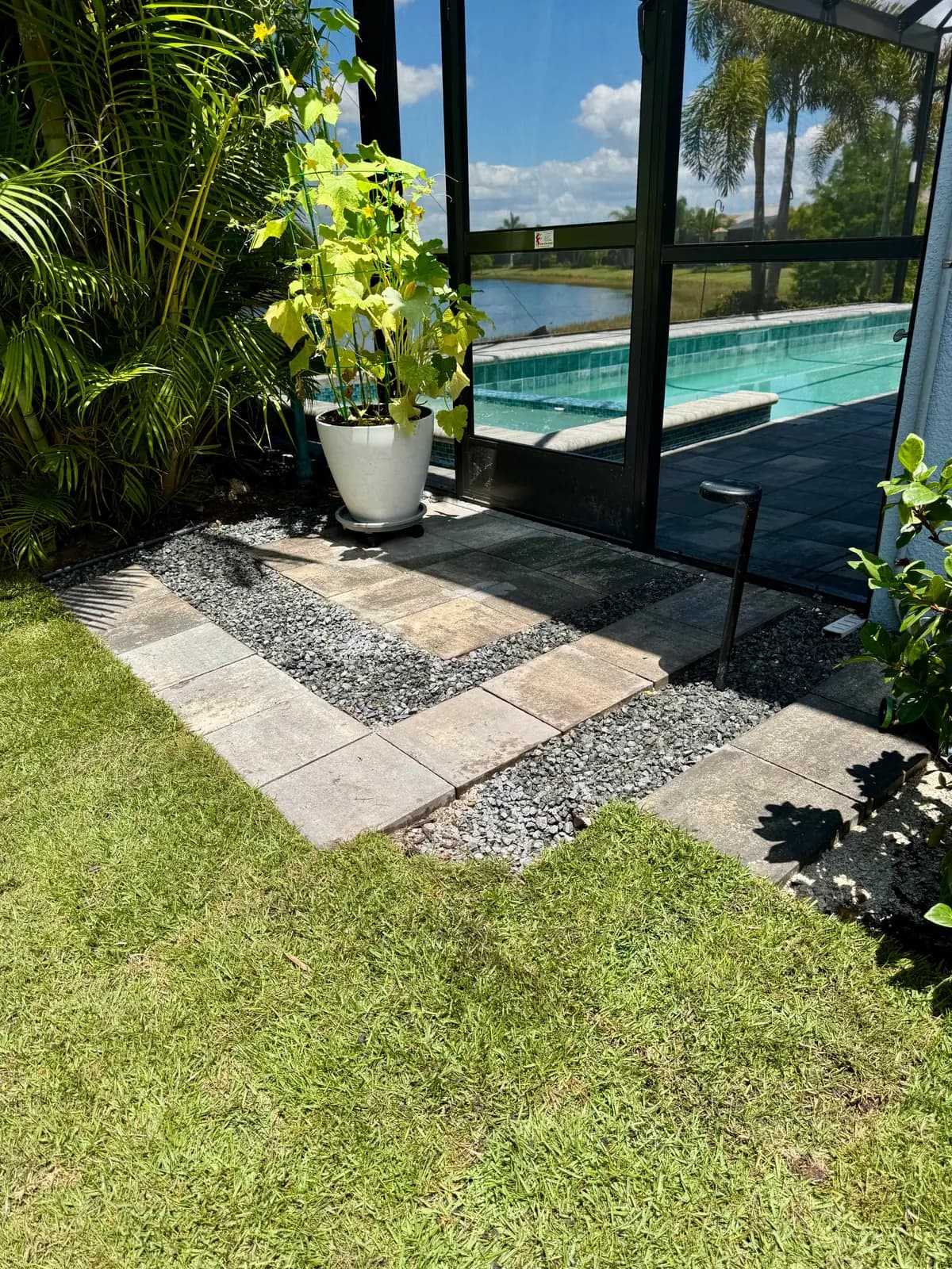 Paver border and river rock strip beside newly laid sod, with a pool and lake behind